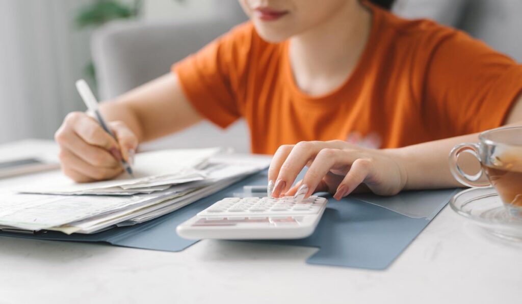 Woman calculating and compiling multiple outstanding debts, considering if she should take an urgent cash loan in Singapore