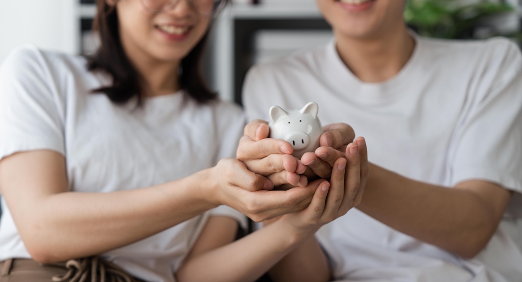 A couple in matching white tees holding a piggy bank, in unison agreement of their financial decisions