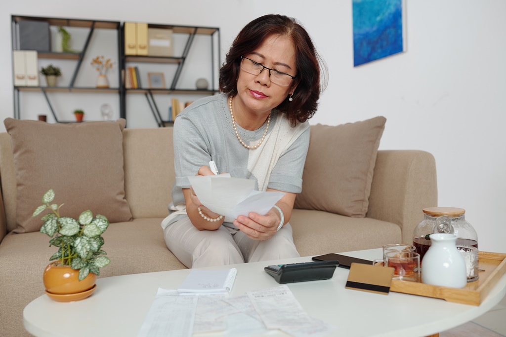 Middle aged woman counting multiple debts with pen and calculator at home, wondering if loans for bad credit would help her